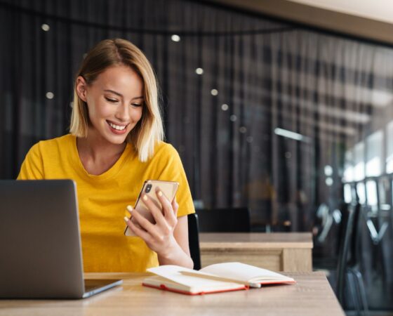 Smiling-woman-using-mobile-phone-laptop