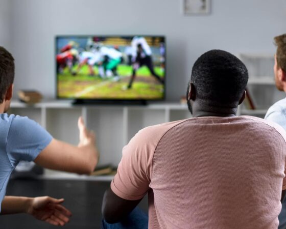 Male friends gather to watch football competition on big screen, sofa experts